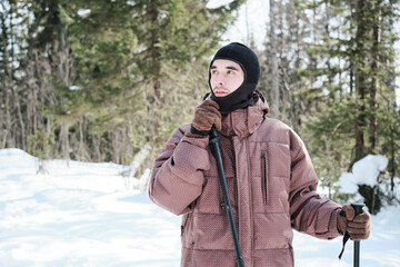 Fototapeta na wymiar Portrait of young Caucasian man wearing balaclava hiking or skiing in local forest on sunny winter day looking away