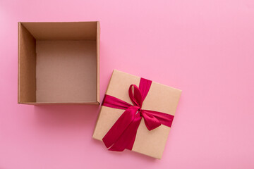 open empty gift box with a lid with a satin bow lying next to it on a pink background with copy space