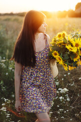 Beautiful woman holding sunflowers in warm sunset light in meadow. Tranquil atmospheric moment in...