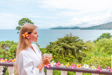 Fototapeta na wymiar Summer travel vacation concept. Happy traveler woman with cup of hot coffee enjoy and relax on villa terrace with sea view on Phuket island, Thailand.