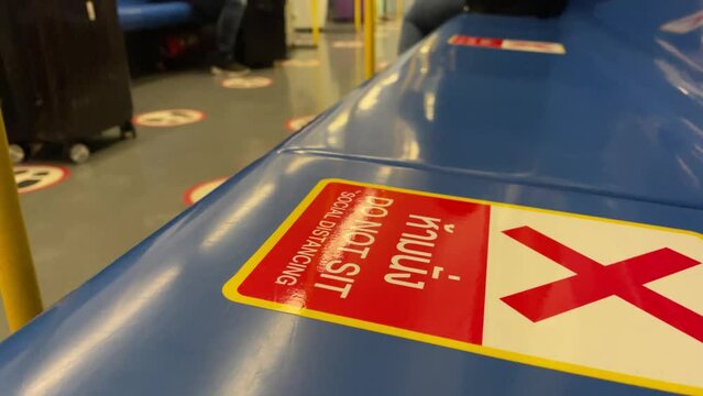 BANGKOK, THAILAND - Circa January, 2022: "DO NOT SIT SOCIAL DISTANCING" sticker on blue seat on moving Airport Rail Link Train. Blurred passengers in background. Close up shot red cross symbol