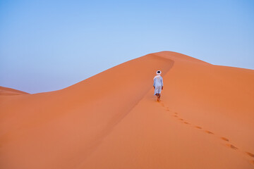 Fototapeta na wymiar From behind a Berber climbing a dune at sunset