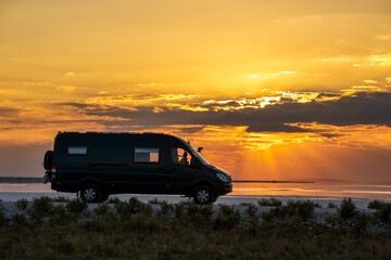 Backlit silhouette of a 4x4 camper van in a desert landscape at sunset
