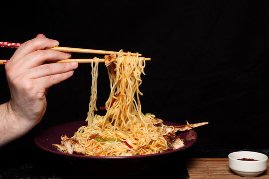 Hand holding chicken noodles with vegetables.Dark background.