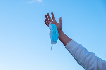 A hand raising a mask against the sky in the background after completing the obligation to wear it.