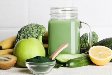 green smoothie in glass bottle, spirulina powder, vegetables and fruits on white ceramic tile...