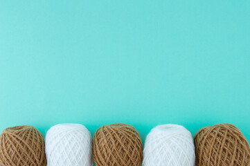 White and brown skeins of yarn in  row. Turquoise background. Place for text.