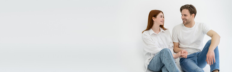 Positive young couple holding hands while sitting on white background, banner.