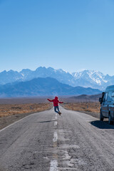 Boy or girl jumping in the middle of the road with a campervan at the side. Overland travel by...