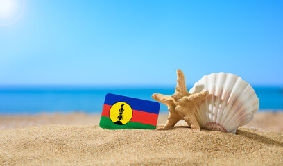 Fototapeta na wymiar Tropical beach with seashells and New Caledonia flag. The concept of a paradise vacation on the beaches of New Caledonia.