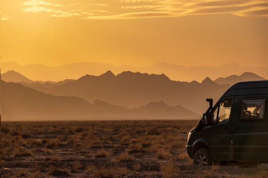 Rugged reliefs of the mountains in the Iranian desert at sunset with a 4x4 camper van on the side