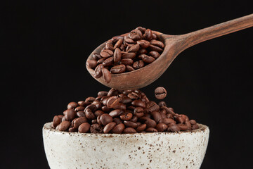 Putting coffee beans from a wooden spoon into a pile in a bowl on a black background.