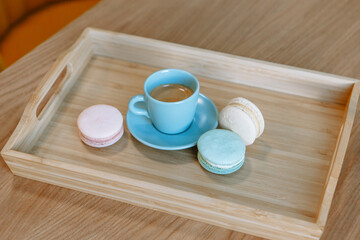 A cup of blue coffee standing on a wooden tray. Macaroons are lying nearby