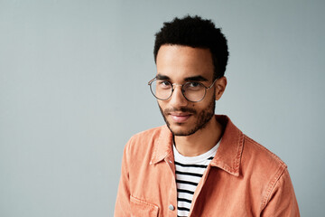 Obraz premium Portrait of smiling handsome young Afro American man in round glasses and casual shirt standing against isolated background
