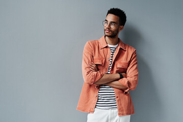 Obraz premium Contemplative young black man with stubble standing with crossed arms against gray wall