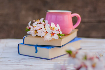 a pink cup and a blooming spring twig of an almond tree on a stack of books on the table. spring still life