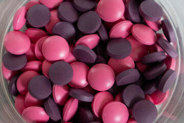 A lot of pink and lilac round-shaped tablets in a close-up in a glass, a high-quality photo.
