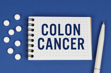 On a blue background, a pen, tablets and a notepad with the inscription - COLON CANCER