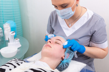 The cosmetologist treats the skin of the face with a tonic