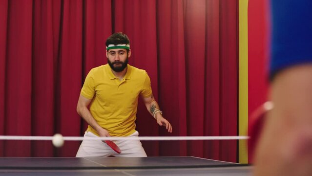 Handsome with a large smile guy playing with his friend on the ping pong game he wearing table tennis uniform he catch the balls and hitting at the same time. Shot on ARRI Alexa Mini