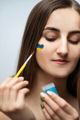 A young girl with beautiful skin draws a heart from the colors of the Ukrainian flag, no war