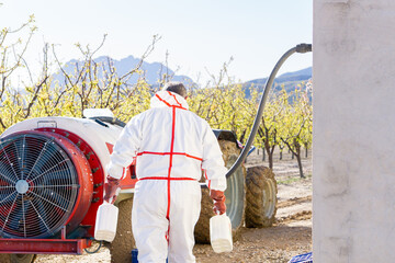 Farmer preparing a sprayer with chemicals to be applied to the field - obrazy, fototapety, plakaty