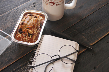 Banana Cake on a black wooden table With note book, glasses, and coffee mugs.