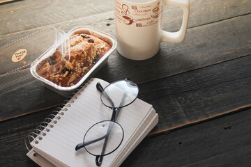 Banana Cake on a black wooden table With note book, glasses, and coffee mugs.