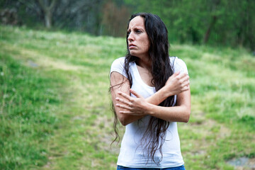 long-haired brunette girl in the rain hugging herself, feeling lonely. Looking to the side, with room to copy. mental health concept. sadness, depression and suicide. bad mood.