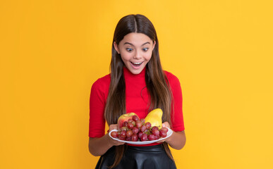 cheerful amazed child hold fresh fruit plate on yellow background