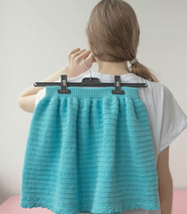 The girl stands with her back and holds a hanger with a knitted blue skirt in her hand