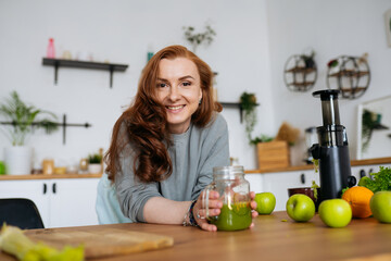 portrait A red-haired woman with long hair made a green smoothie from fresh vegetables and fruits...