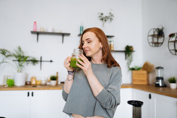 young woman with long red hair drinks green freshly squeezed juice