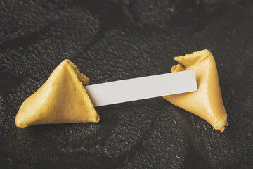 Open chinese fortune cookie with blank white paper on dark background.