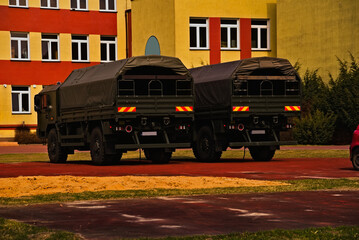 Wojskowe ciężarówki terenowe ( of road ) polskiej produkcji parkujące przodem do budynku dawnej szkoły . - obrazy, fototapety, plakaty