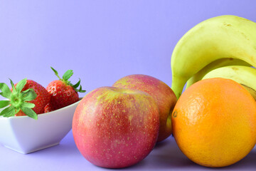 Varied fruit, full of vitamins and benefits for our health, orange, banana, apple and strawberry, mauve background. Copy space.