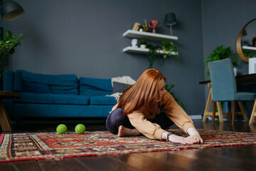 Obraz na płótnie Canvas a red-haired woman in a tracksuit does exercises in the living room