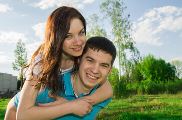 Obraz premium A young man carries his beautiful smiling woman on his back in the park. Couple in love having fun together.