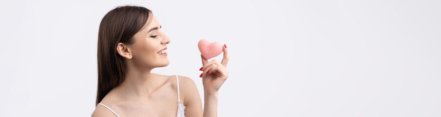 Beautiful smiling woman with clean skin, natural make-up and white teeth on a gray background. Holding a pink hygienic heart.