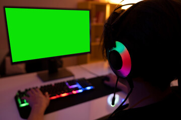 Green computer screen, selective focus on teenage headset using computer in a dark room. Teenage wearing a headset with a mic, dark room with warm led lights.