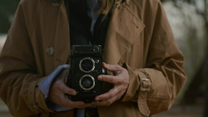 Young attractive blonde female hold, make photo using tlr retro vintage medium format 120 mm film camera outside at beautiful forest during weekend, vacation, wearing casual beige coat, eyeglasses - Powered by Adobe