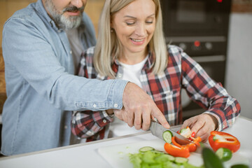 Close up of caucasian mature couple chopping fresh vegetables on board and having fun on kitchen. Concept of family and culinary.