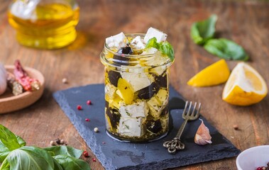 Appetizer, marinated feta with spices and olives in oil in a glass jar on a wooden background.