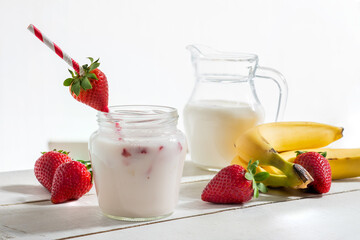 Strawberry and banana yogurt in jar with straw with strawberry on white wood with strawberries and bananas