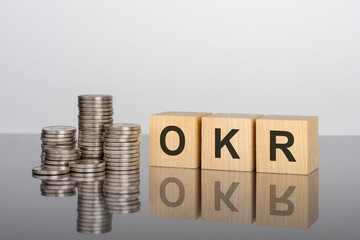 okr - text on wooden cubes on a cold grey light background with stacks coins