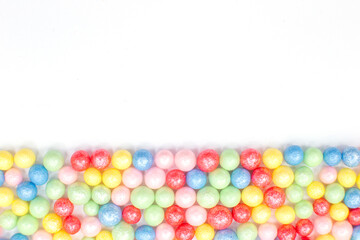 Multi-colored round glossy balls of sugar confectionery topping lie at the down on a white background.