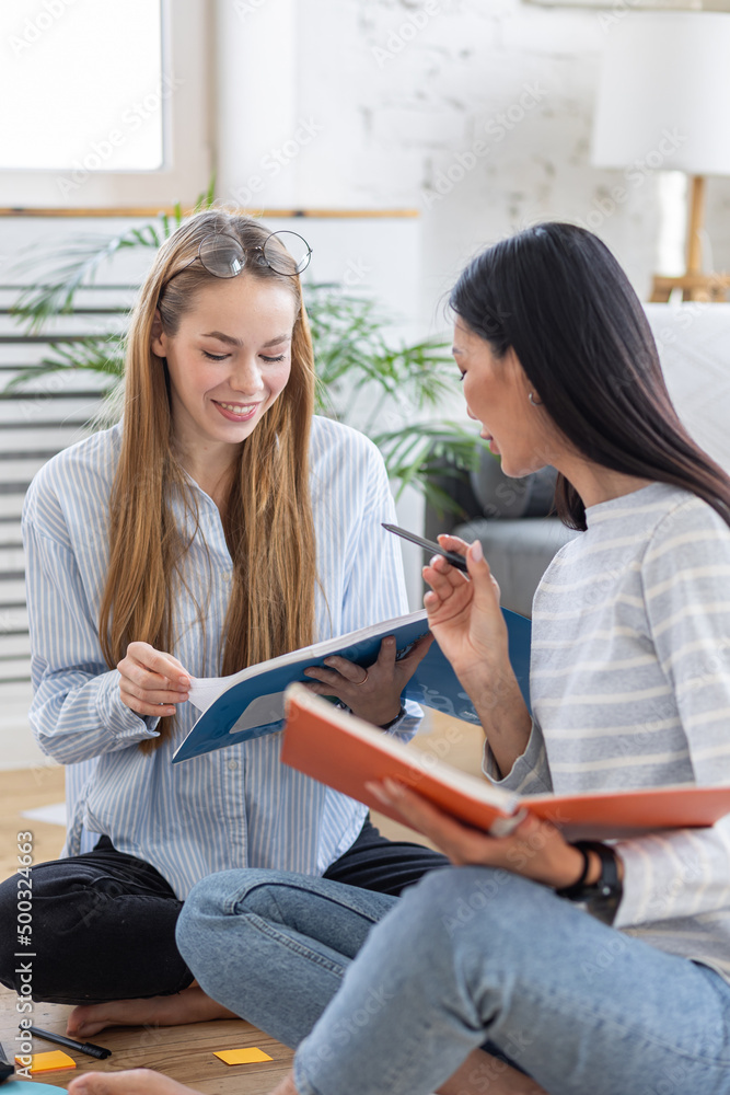 Wall mural two young girls learning foreign languages together at home sitting on the floor. college life, stud