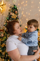 grandmother holds her grandson in her arms near the Christmas tree