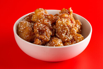Bowl of Sesame Chicken on a Bright Red Background