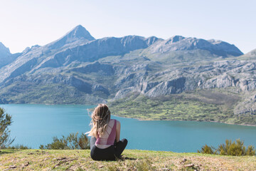 Fototapeta premium Chica joven relajada y sentada en el cesped observando la montaña en modo zen